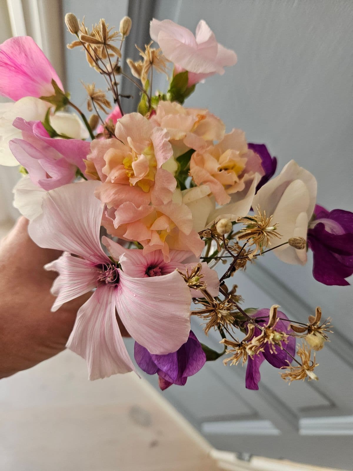 En håndholdt bukett med rosa, hvite og lilla blomster og noen tørre frøstander.